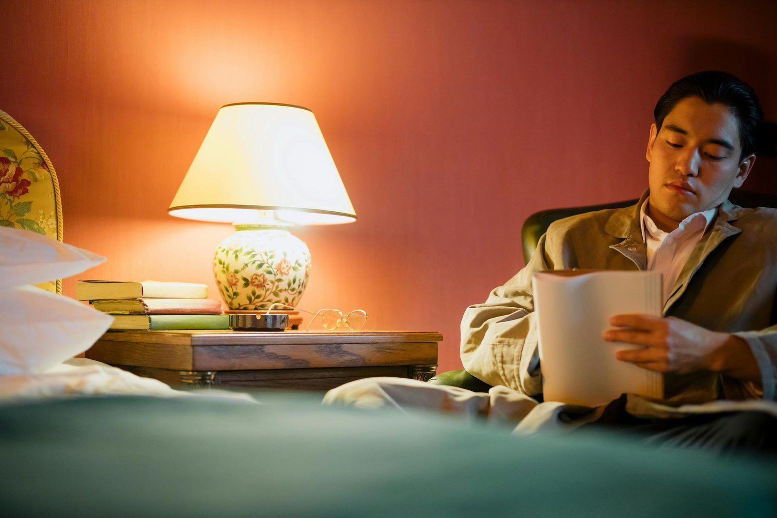 Stay Calm 1 An adult man reads in a warmly lit hotel bedroom with a lamp and bedside table.