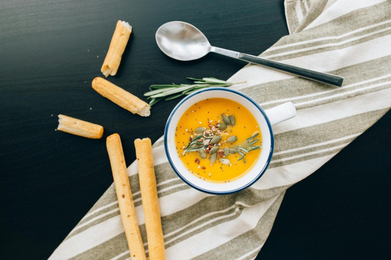 Cook the Soup Slowly 1 Warm pumpkin soup garnished with seeds and herbs, served with breadsticks. Perfect for a cozy meal.